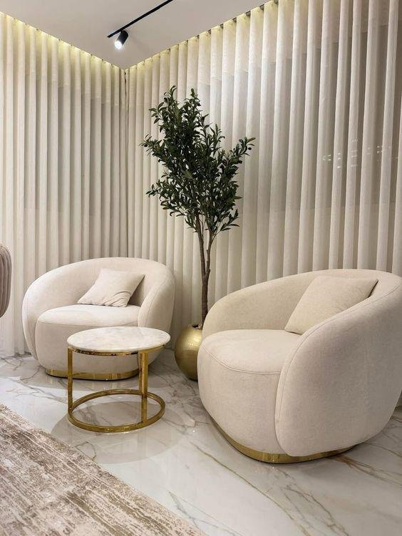 Styled corner with curved cream chairs, olive tree and marble side table