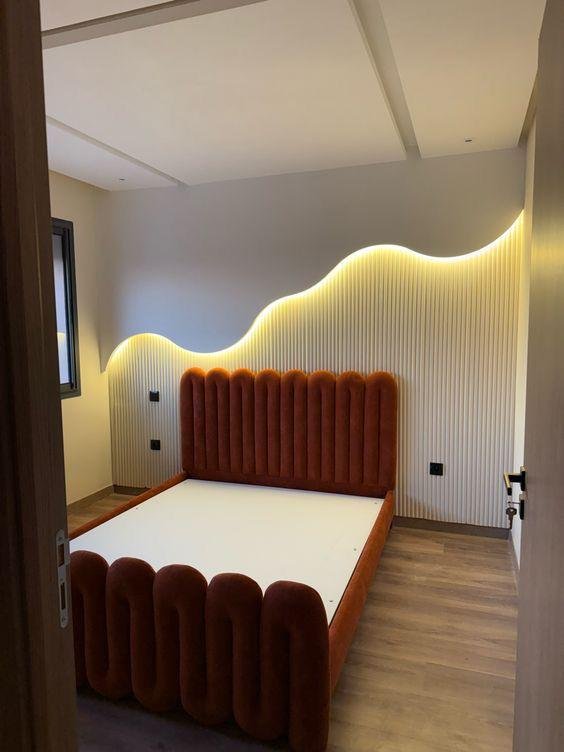 Bedroom with rust velvet channel-tufted bed and wave-lit slat wall